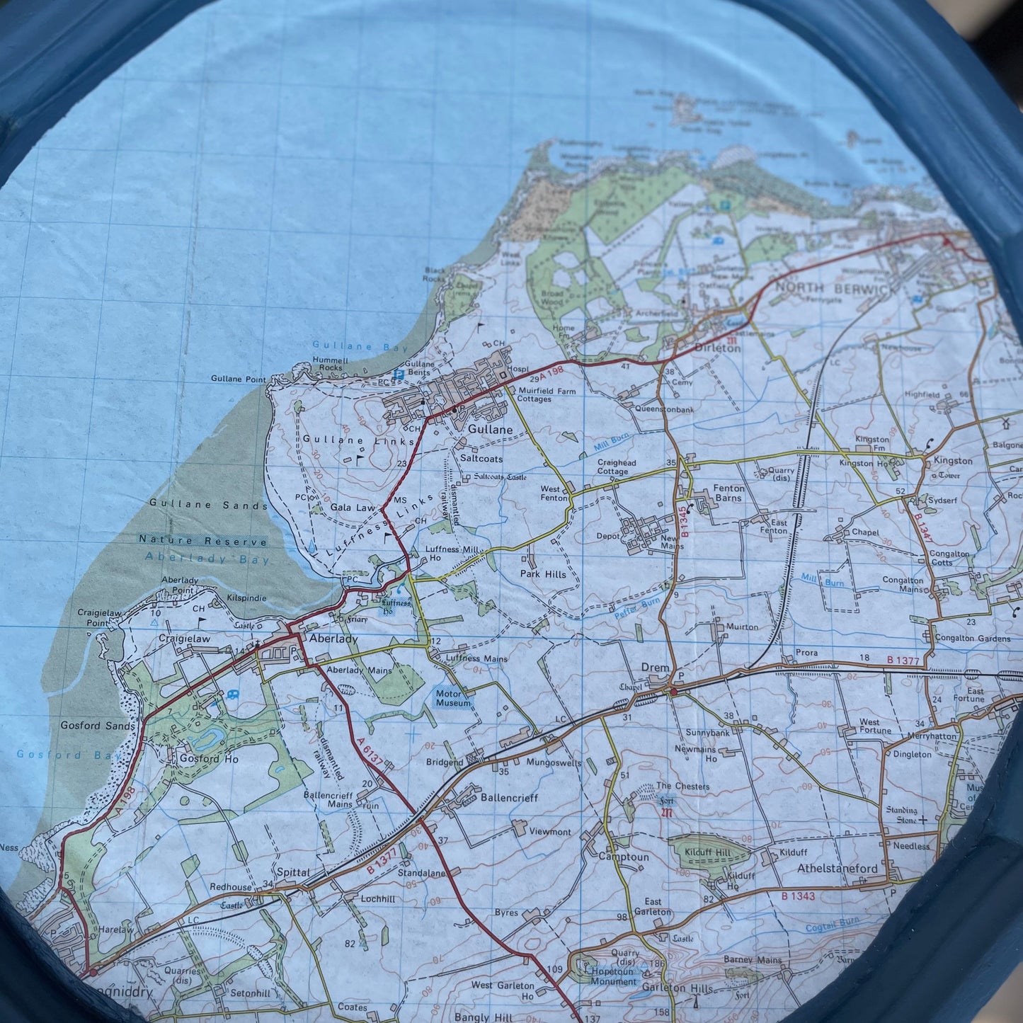 Map of a coastal area with roads and green spaces, viewed through a circular lens.