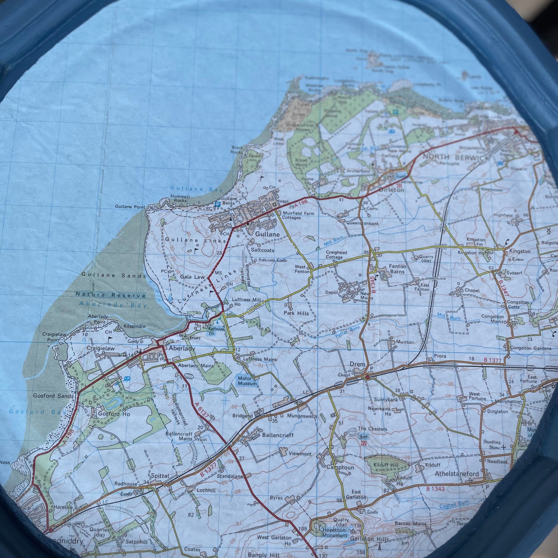 Map of a coastal area with roads and green spaces, viewed through a circular lens.