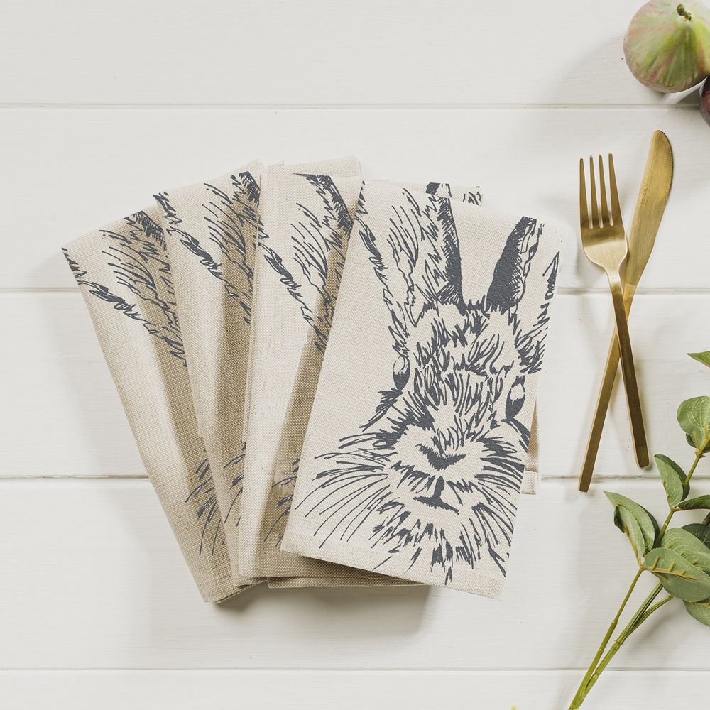 natural off white brown linen and cotton square napkin with black screen printed hare rabbit illustration on table with gold cutlery 